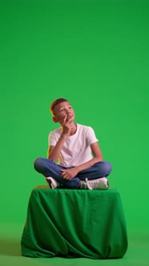 Pensive Boy Sitting on a Stool on a Green Screen