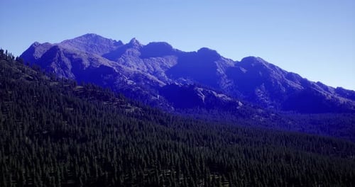 Majestic Mountain Range Under a Clear Blue Sky with Dense Forest Below