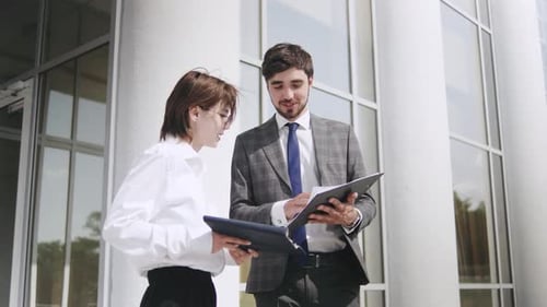 Business Professionals with Tablet Discuss Project Details Outside a Modern Office Building on a