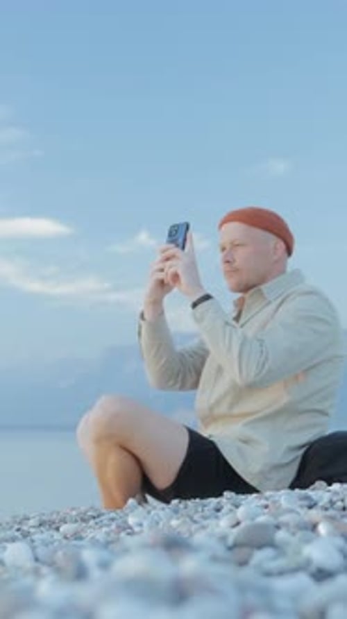 Man Taking Multiple Smartphone Photos While Sitting on Beach