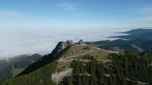Aerial view of mountaintop lodge above rolling hills and sea of clouds under blue sky