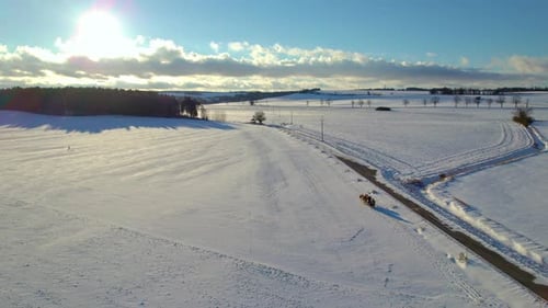 Horse-drawn winter sleigh in a beautiful snowy landscape with sun shining through the clouds