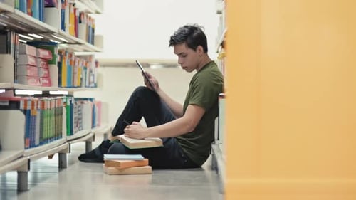 Male Freshman Sitting on Library Floor while Preparing for Future Project