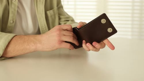 Poverty. Man taking out dollar banknote from wallet at white table, closeup