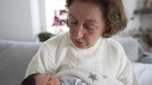 Grandmother gazing lovingly at her newborn grandson, close-up, intimate and tender family moment,