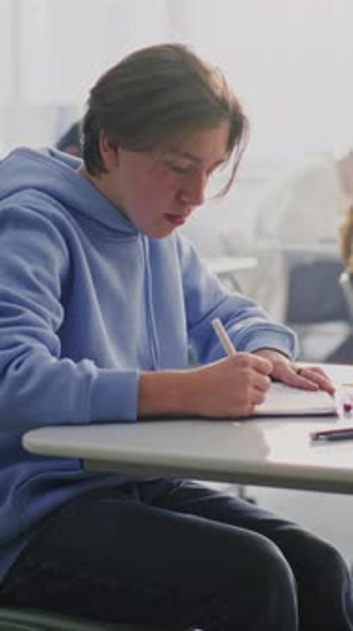 Teenager Writing at Desk in School Classroom