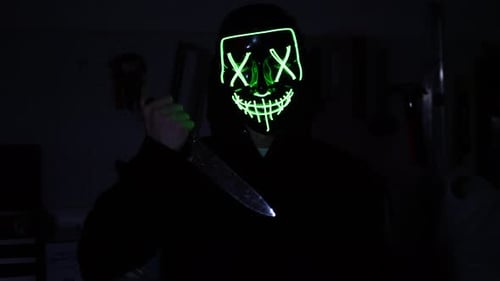 Person with Glowing Mask Holds Knife in Dark