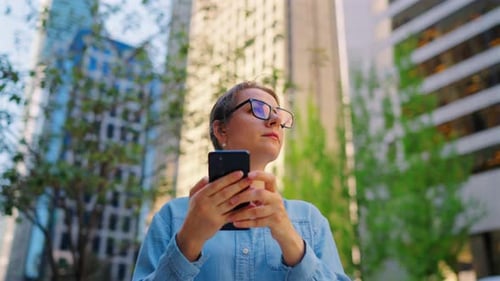Caucasian Woman in Glasses Standing on the Street and Using Smartphone