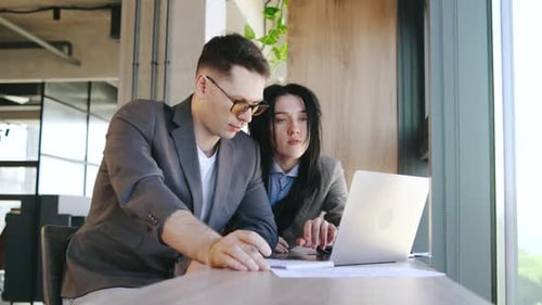 Two Business Professionals Have a Productive Discussion Over a Laptop in a Modern Office Sharing