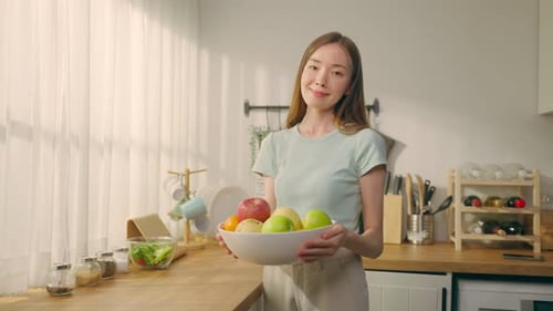 Smiling Woman Holds Fruit Bowl in Bright Kitchen
