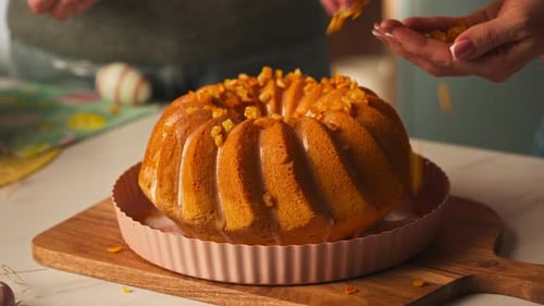 Kandierte Orangenstücke von Hand über den glasierten Osterbundtkuchen in einer Tarteform streuen. Nahaufnahme