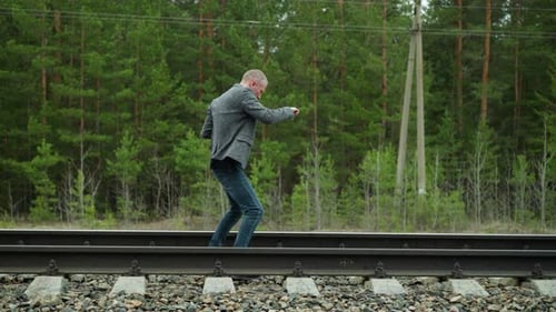 Determined Man in Grey Suit Practicing Taekwondo Along Railway Tracks in Forest