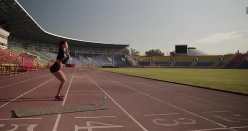 Sportive Female Sprinter Exercising with Weight in Stadium