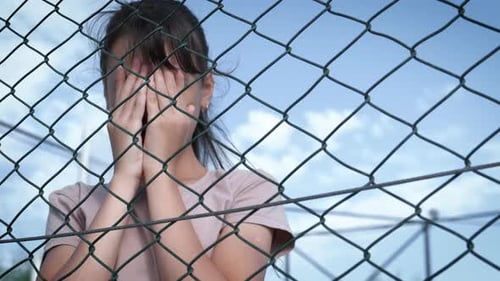 Child Covers Face near Chain Link Fence on Sunny Day