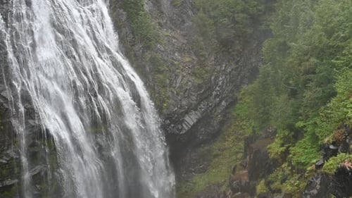 Aerial view of dramatic waterfall cascading down forested cliffside in remote mountain wilderness