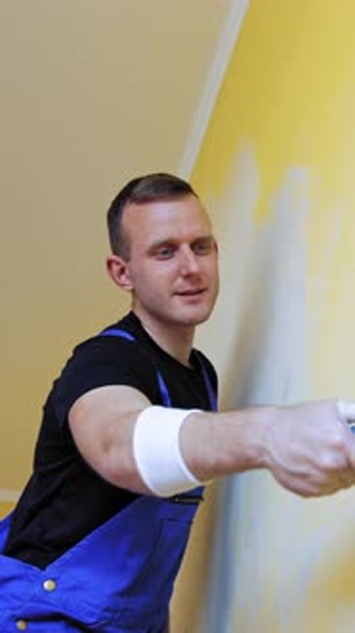 Attraktiver Maler, der eine neue Inneneinrichtung der Wand anfertigt. Fröhlicher Mann, der mit Gemälden arbeitet. Vertikales Video