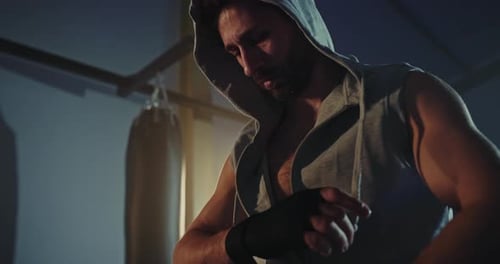 Boxer Wrapping Hands in Dark Gym Before Training