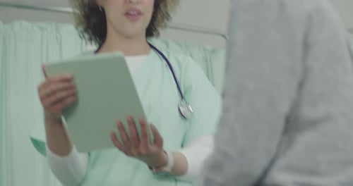 Female Nurse Examining Senior Patient in Hospital, taking notes on Digital Tablet