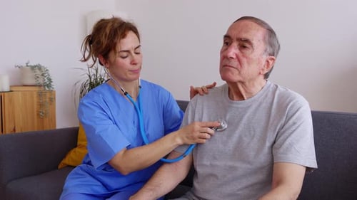 Young Female Doctor Listening Heart Sound to Disabled Older Patient at Home