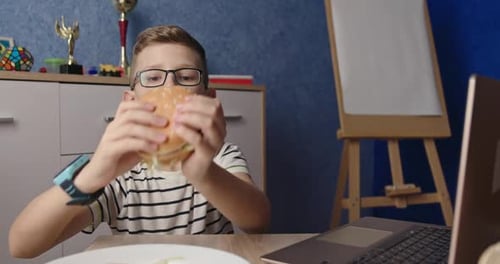 Young Boy Eating Hamburger at Table Indoors