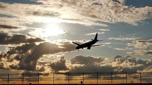 Passenger Airplane Landing at Sunset Over Airport Fence