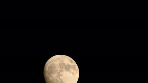The moon is obscured by some clouds as it rises.