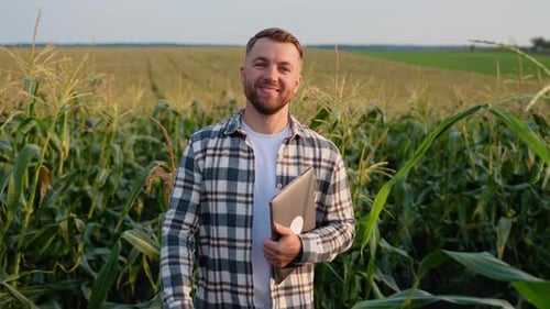 Smiling Man Holding Laptop in Cornfield