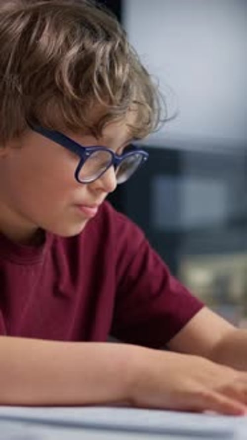Junge mit Brille konzentriert sich darauf, ein Buch oder eine Zeitung in einer Innenumgebung zu lesen oder zu studieren