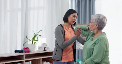 Young Woman Helping Senior Woman Exercise Arm Indoors