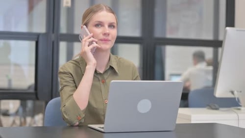 Woman talking on phone working at desk on laptop
