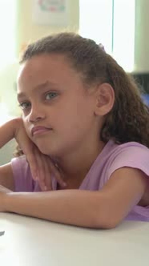 Vertical video: Opening eyes, tween girl in lilac shirt shifting gaze in classroom studying laptop