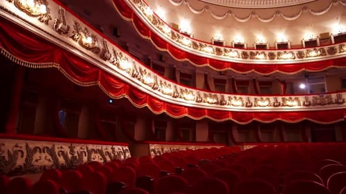 Panoramic view of beautiful richly decorated theater hall. Rows of red chairs in theater hall.