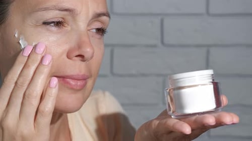 Woman Applies Cream To Her Face In Close Up