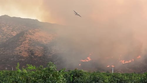 Firefighters plane flying over grey smoke, coming up from a wildfire burning. Fairview Fire in Hemet