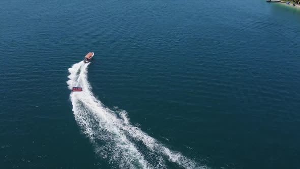 Aerial tracks boat towing raft of happy tourists on bright sunny day ...