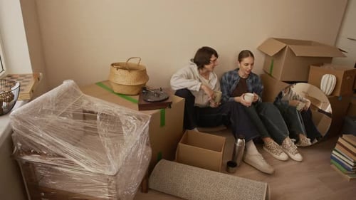 Young Couple Resting among Packed Boxes after Moving into Apartment