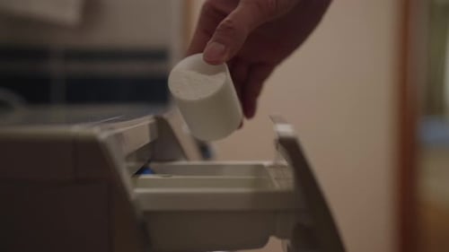 Gros plan de la main plaçant une capsule de détergent pour machine à laver dans le compartiment désigné de la machine à laver
