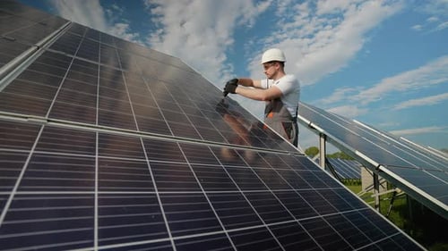 Engineer Repairing Solar Panels with a Drill Under the Sun