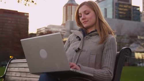 Woman Sits On Park Bench Using Laptop Computer