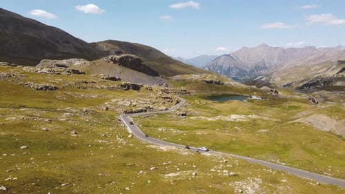 A drone rises in breathtaking mountain scenery and shows driving cars arriving at a mountain lake.