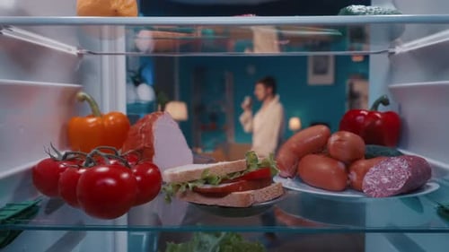 Refrigerator with Vegetables Sausage and Sandwich on the Shelves Inside View The Door Opens a Man in
