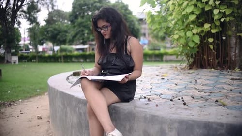 Ein heißes asiatisches Mädchen studiert auf dem Campus des University College und schreibt in ein Notizbuch unter einem Baum