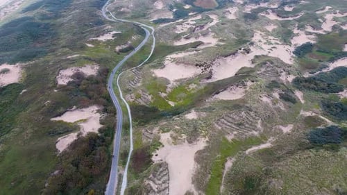 Aerial view of a coastal landscape with lush greenery sandy dunes and winding road running parallel