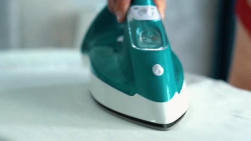 Close Up Shot of Hand Irons Clothes with a Steam Iron on an Ironing Board Indoors