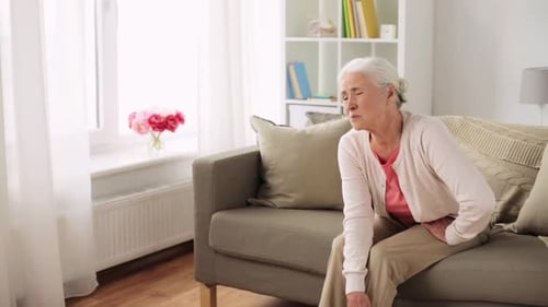 Senior Woman Massaging Knee on Sofa at Home
