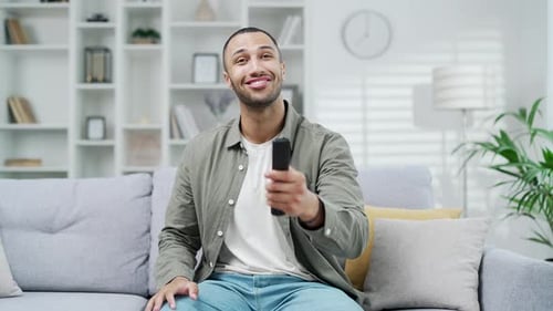 Webcam view A man looks at camera of the TV screen and switches channels or programs with the remote