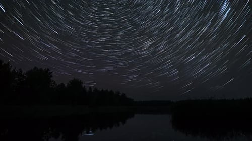 Kometenförmige Sternspuren am Nachthimmel über dem See