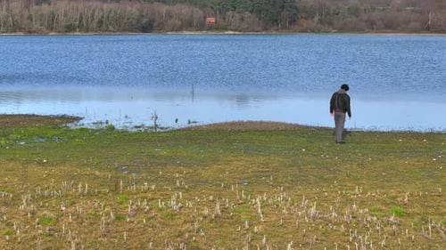 A Man Is Walking Alone Towards Calm Lake During Daytime. Aerial Drone Shot