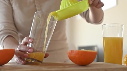 Woman Pours Fresh Orange Juice into Glass