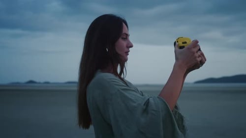 Woman with Retrostyle Camera at Beach Young Woman is Standing on Beach at Dusk Taking Pictures or